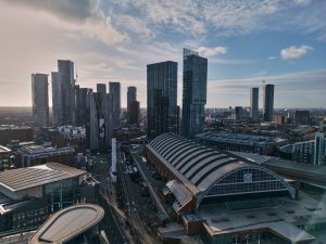 Aerial view of a cityscape with tall buildings and a large, arched roof structure under a clear sky.