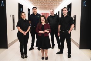 A team of five smiling professionals stands in a bright hallway, ready for a cleaning project.