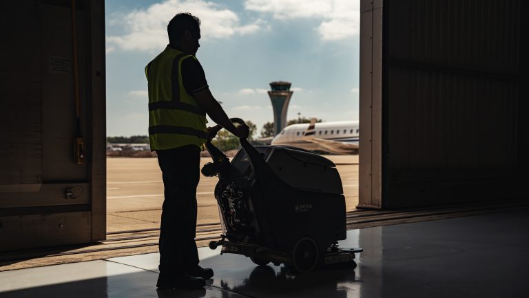 A man operating a scrubber dryer in an airport hanger