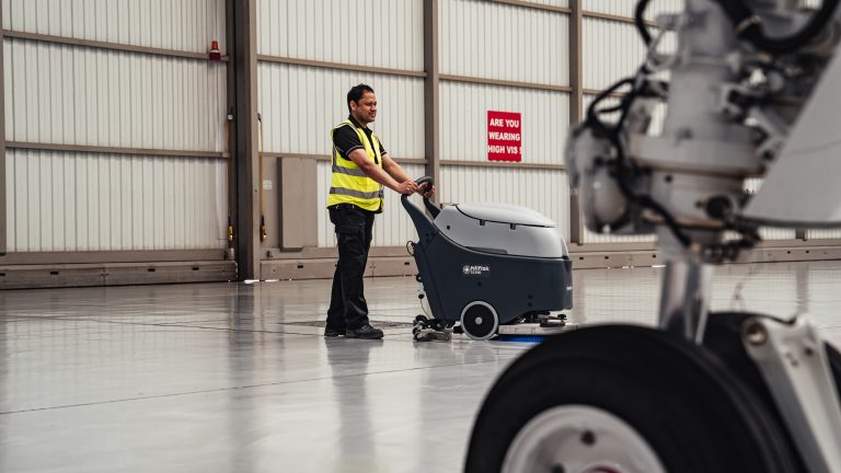 Cleaner in high-vis using a scrubber dryer in an airport hanger